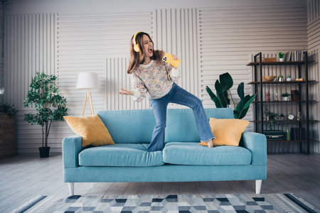 Young woman enjoying music while dancing and standing on a couch at homeの写真素材