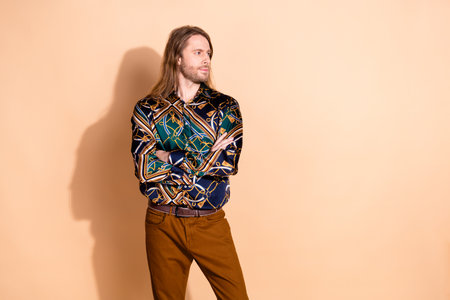Trendy young man with long hair wearing a patterned green shirt, standing confidently against a beige backgroundの写真素材
