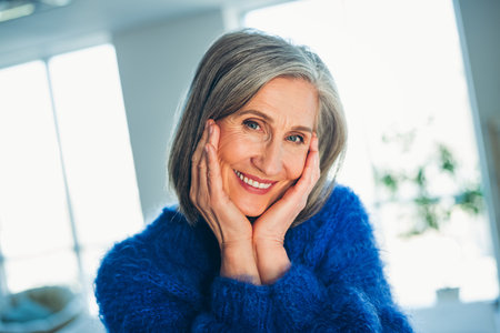 Smiling mature woman in cozy sweater posing in a comfortable home environment with stylish gray hair and natural charmの写真素材