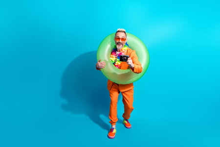 Charismatic man in orange suit with sunglasses and inflatable ring showing a camera against a...