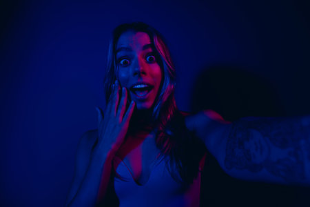 Young woman posing with shocked expression in neon blue and pink lighting