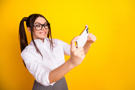 Teenager in formal wear enjoying smartphone on yellow background, representing youthful fun and modern lifestyleの写真素材
