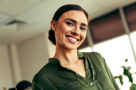 Smiling businesswoman in a green blouse posing confidently in a bright office setting, representing professionalism and successの写真素材
