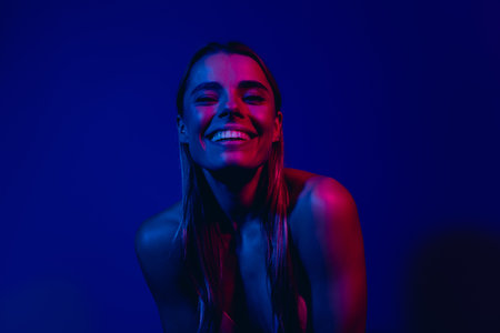 Young woman smiling in vibrant pink and blue neon lighting suggesting energy and confidenceの写真素材