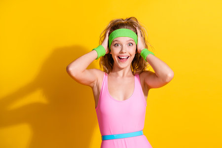 Happy young woman in vibrant activewear poses energetically against a bright yellow background...