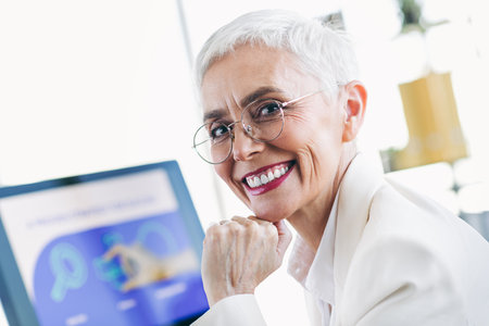 Confident mature businesswoman in professional formalwear engaging in office work with a cheerful smileの写真素材