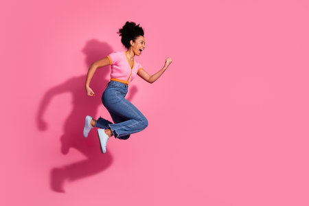 Energetic young woman in stylish casual wear jumping against a vibrant pink background, expressing joyの写真素材
