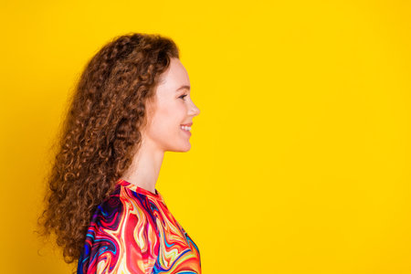 Side profile of a young woman with curly red hair against a vibrant yellow background in trendy...