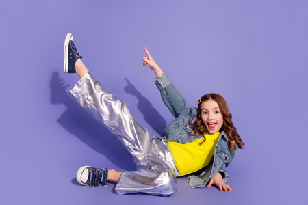 Energetic young girl posing stylishly in a vibrant outfit with a playful gesture against a purple...