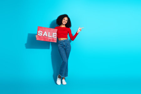Happy young woman in stylish casual clothes joyfully promoting a sale on a blue background while pointing with enthusiasmの写真素材