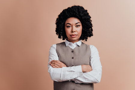 Confident young businesswoman in stylish formal attire posing against beige background, exuding professionalism and successの写真素材