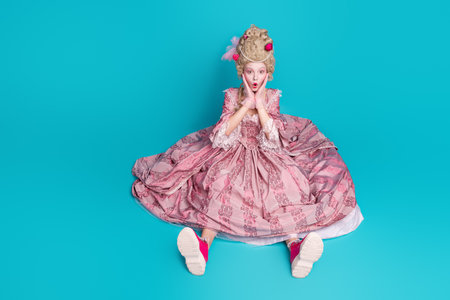 Photo of charming lovely lady princess wear pompous pink ruches gown corset sit floor isolated on blue color backgroundの写真素材