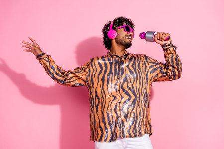 Young Stylish Man Singing with Microphone in Vibrant Outfit on Pink Background, Expressing Joy and Music Enthusiasmの写真素材