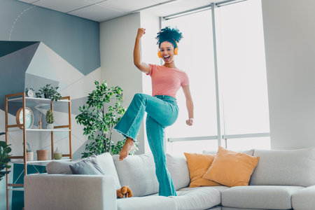 Joyful young woman enjoying music and movement in a bright living room with modern decor and natural lightの写真素材