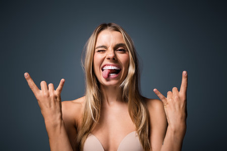 Confident young woman playfully posing with rock gesture against neutral backgroundの写真素材