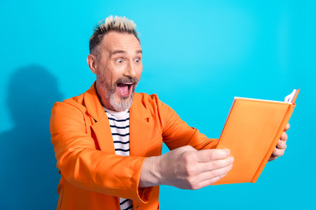Excited mature man reading an orange book against a blue background while wearing a bright orange...