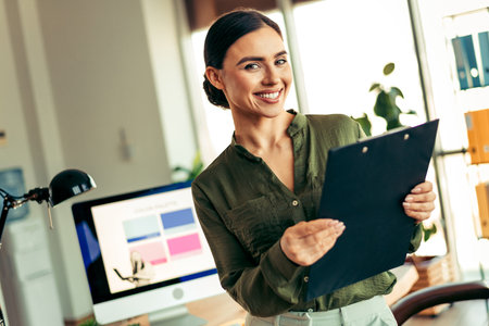 Confident young businesswoman holding a clipboard in a bright modern office environmentの写真素材