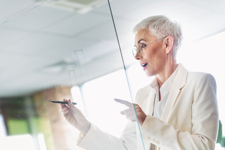Confident senior businesswoman working on strategy in a modern office environment promoting organizational success and growthの写真素材