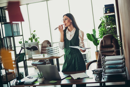 Confident businesswoman standing in an elegant office holding documents and speaking on a phone headsetの写真素材