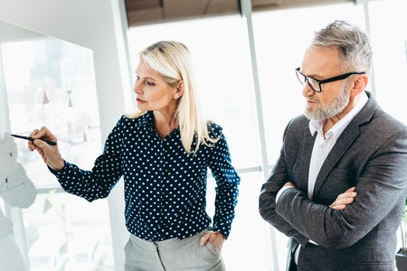 Business professionals collaborating indoors, mature colleagues discussing ideas in modern office during a daytime workplace meetingの写真素材
