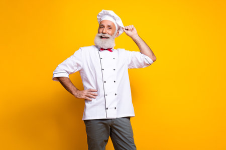 Smiling senior chef in uniform posing confidently against a vibrant yellow backgroundの写真素材