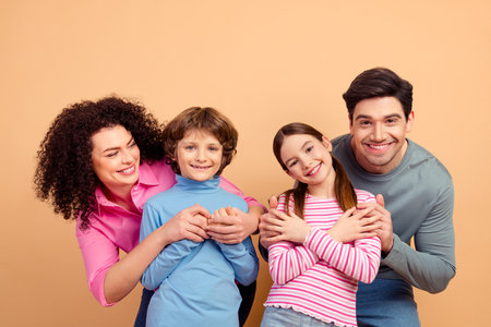 Happy family portrait of parents and two children smiling and bonding together on a beige background