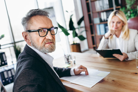 Senior businessman and businesswoman collaborating in professional office environment, engaged in a formal business discussionの写真素材