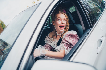 Excited woman in historical dress driving modern car, blending past and presentの写真素材