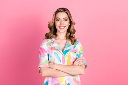 Smiling young woman in a colorful shirt posing confidently with arms crossed against a vibrant pink backgroundの写真素材