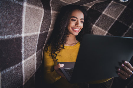Young afro woman studying indoors on her laptop for remote education in a cozy home settingの写真素材