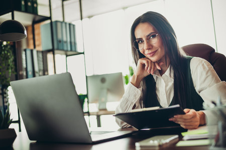 Confident businesswoman in office workspace reviewing documents and working diligently in a bright and professional environmentの写真素材