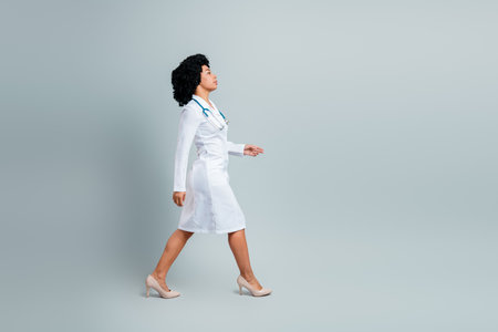 Qualified female doctor walking in uniform with stethoscope on a gray background, representing professionalismの写真素材