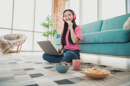 Young woman enjoying leisure time with coffee, snacks, and technology in her cozy living room during a bright daytime.の写真素材