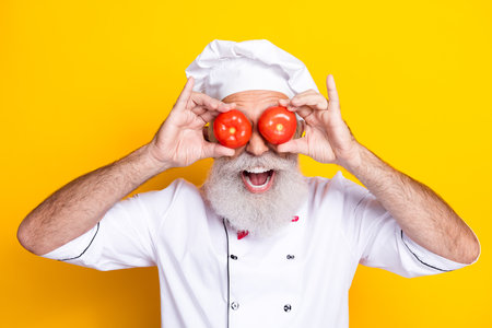Cheerful senior chef posing with fresh tomatoes in front of a colorful backgroundの写真素材