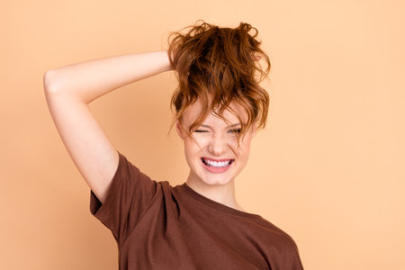 Charming young woman with Auburn hair playfully poses in casual brown t-shirt against a beige backgroundの写真素材