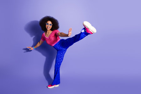 Cheerful expressive woman in vibrant outfit poses energetically in a fun retro style against a purple backgroundの写真素材