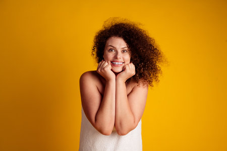 Joyful young woman with curly hair on a bright yellow background, exuding positivity and confidence in a natural and carefree pose.の写真素材