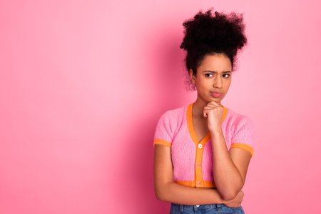 Cheerful girl in casual attire expressing thoughtful pose against a vibrant pink background.の写真素材