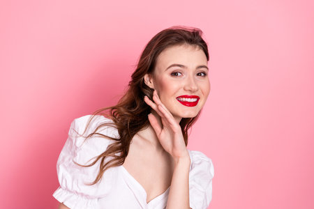 Smiling young woman with red lipstick posing in front of a pink background, showcasing beauty, style, and eleganceの写真素材
