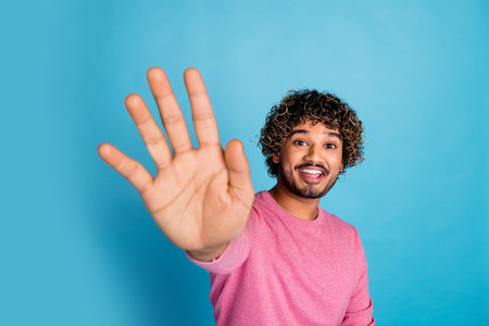 Smiling young man in a pink sweater gesturing with an outstretched hand against a vibrant blue backgroundの写真素材