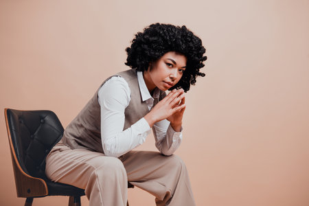 Confident young professional woman posing thoughtfully in stylish formal attire on beige backgroundの写真素材