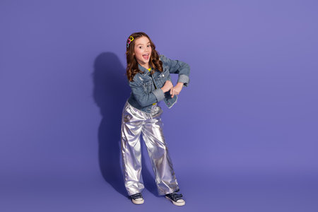 Smiling preteen girl posing confidently in stylish outfit on vibrant purple backgroundの写真素材