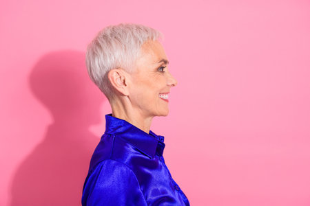 Side profile of a stylish mature woman with a short white hairstyle wearing a blue shirt against a pink backgroundの写真素材