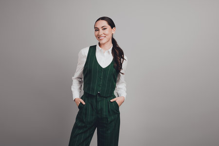 Gorgeous Confident Young Businesswoman in Formal Green Suit Smiling Against Grey Backgroundの写真素材
