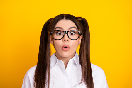 Surprised Teenager With Glasses in White Shirt Against Bright Yellow Background Expressing Shock and Curiosityの写真素材