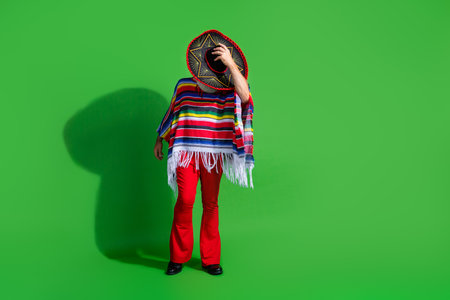 Mature man in traditional Mexican attire with colorful poncho and sombrero against vibrant green backgroundの写真素材