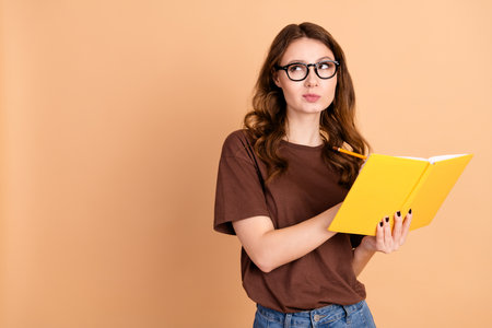 Young woman holding a yellow notebook in thoughtful pose with casual style on beige background