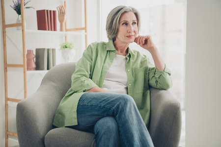 Elderly woman relaxing thoughtfully in a cozy home setting wearing casual attire seated in a...