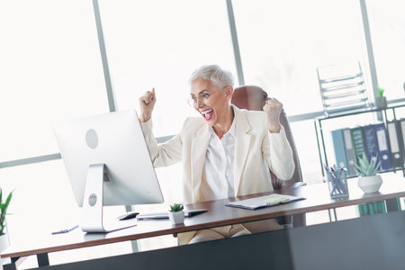 Businesswoman celebrates achievement in modern office space with cheerful enthusiasm and professional attitude in formal attireの写真素材