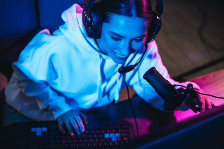 Young woman with headphones and microphone gaming in neon lights highlighting digital entertainmentの写真素材